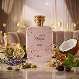 A bottle of Haws For Her GLITZ perfume is displayed on a marble surface surrounded by luxury props including a halved coconut, lime slices, lavender, and spices, with a soft-focus background of a sofa and curtains.